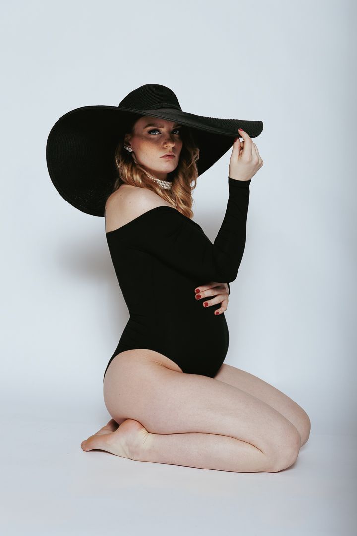 A minimalist artistic nude study featuring a figure in a black hat and top against a white background.