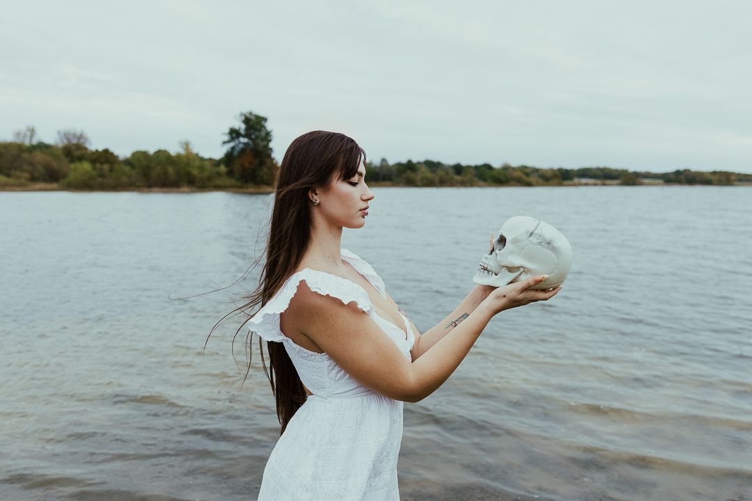 A figure in a white dress stands at the edge of a lake holding a crystal ball, creating a dreamy atmosphere.