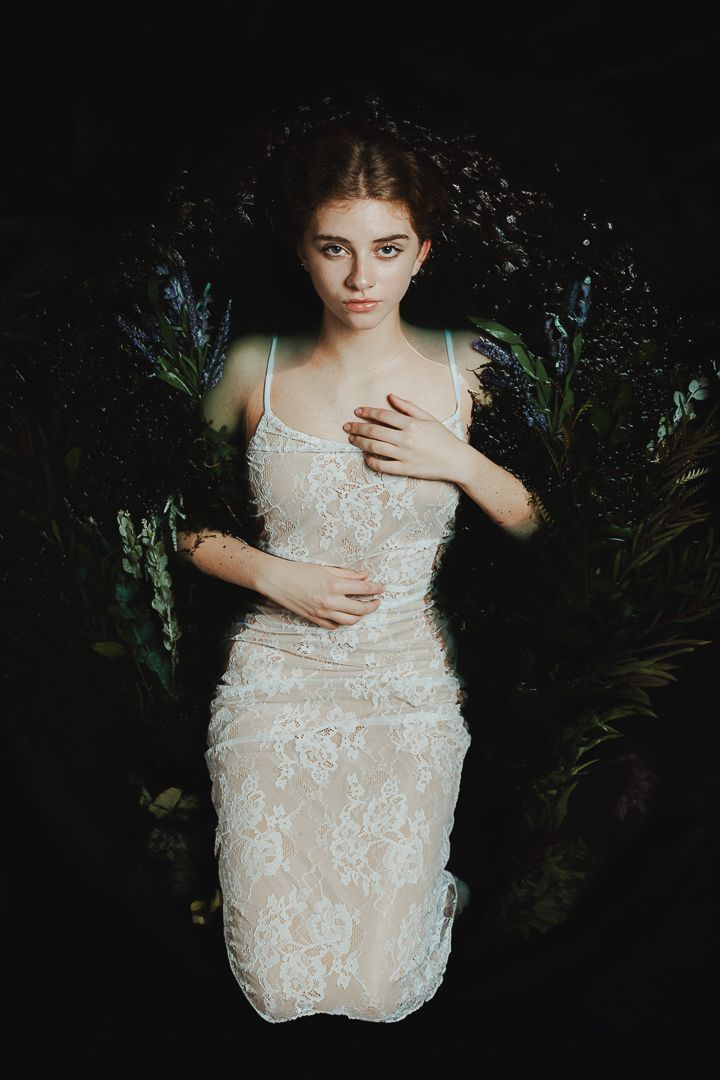 Moody portrait in white lace dress against dark foliage background.