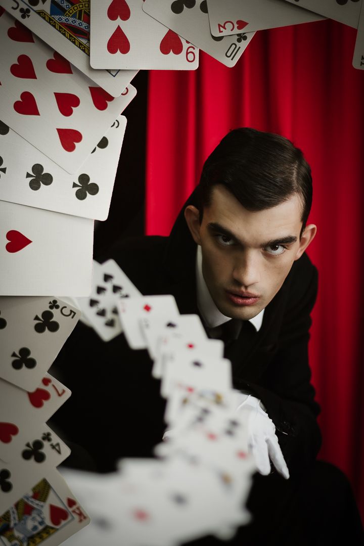 Dramatic playing card themed portrait with red curtain and floating cards creating motion.