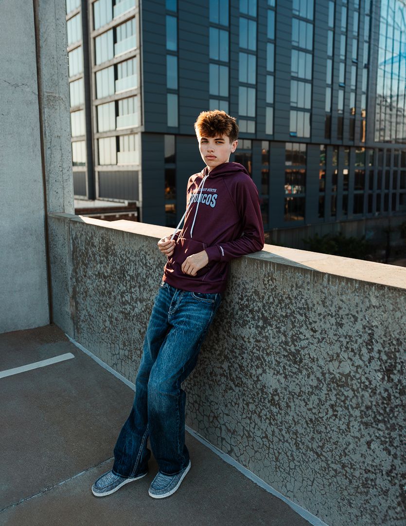 A series of casual urban portraits showing someone in a burgundy sweatshirt and jeans against concrete and glass walls.