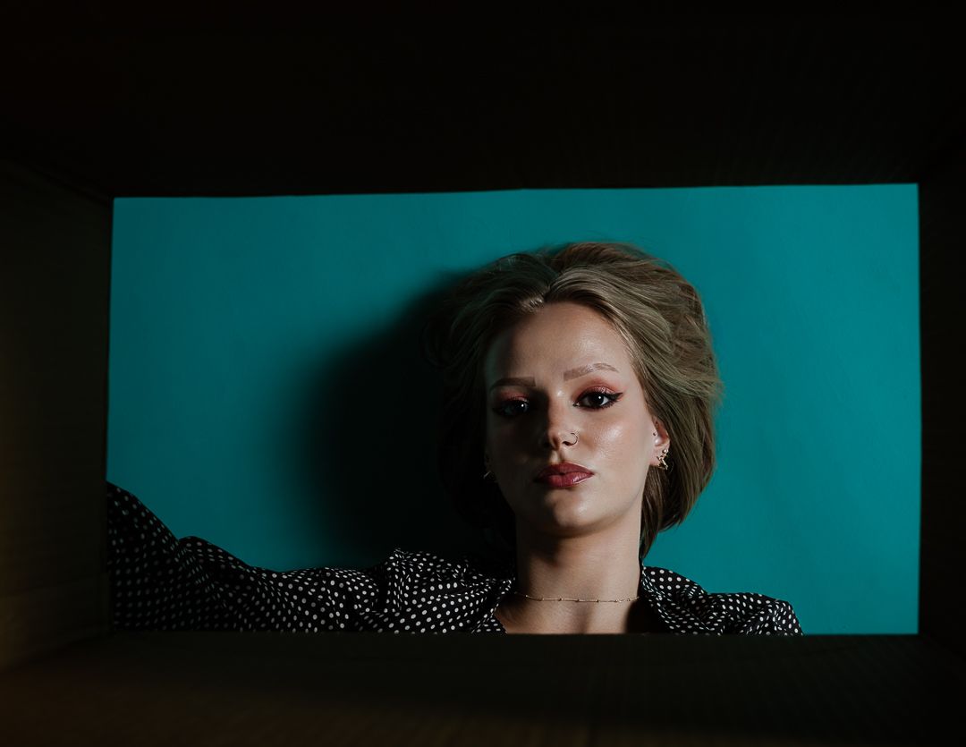 Fashion portrait with polka dot dress against teal backdrop in moody lighting.