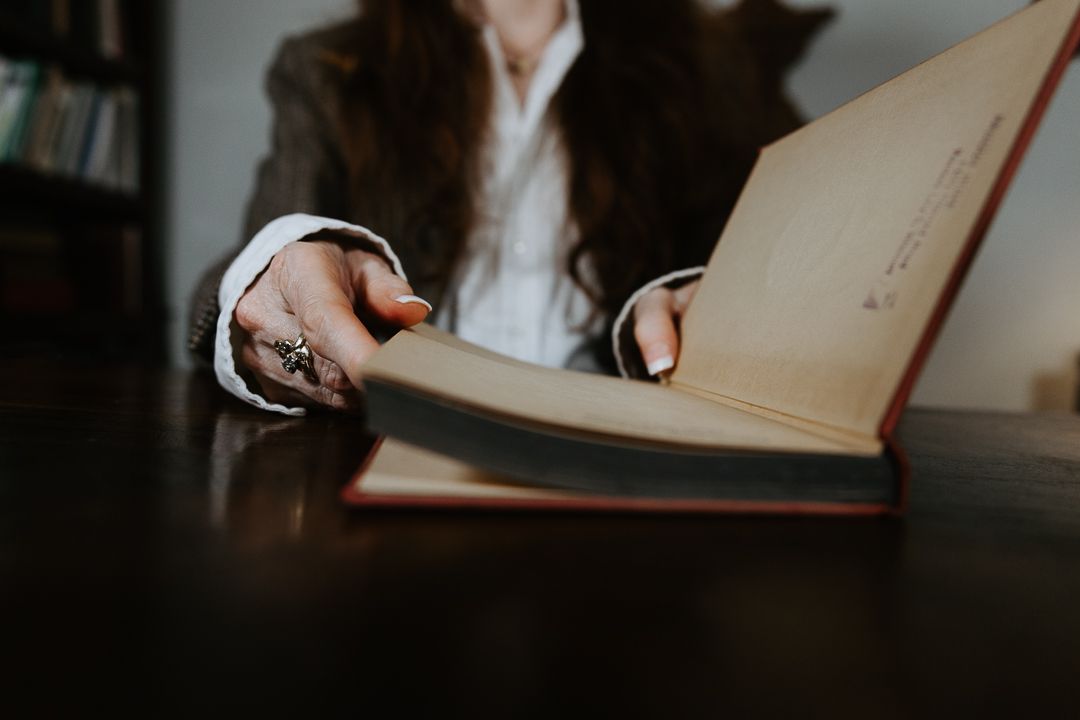 Close-up view of hands writing in an open notebook on a dark wooden desk with blurred background effect.