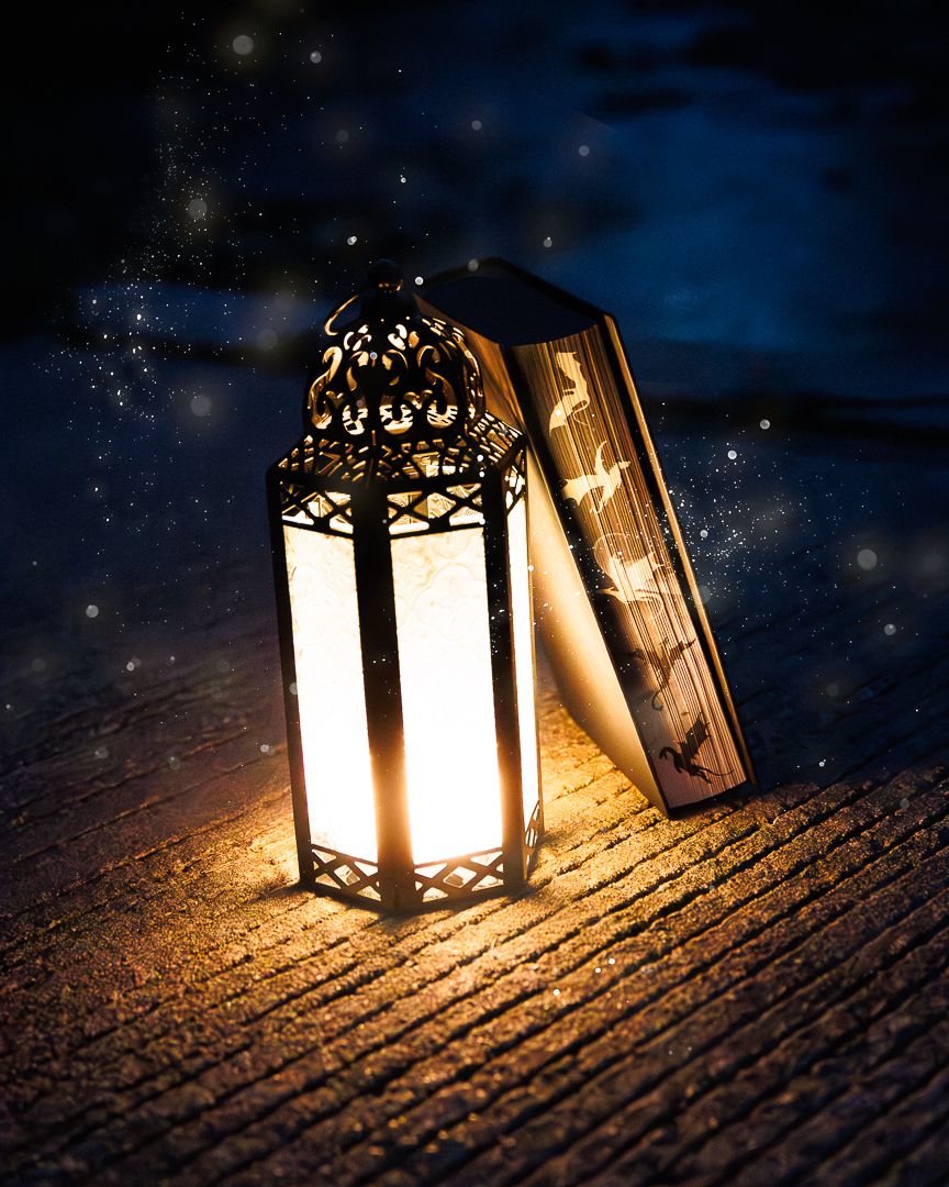 A glowing ornate lantern illuminates an open book on a wooden surface under a starry night sky.