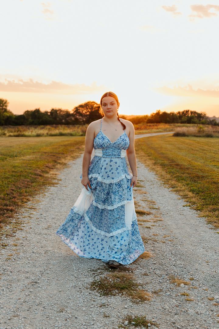 Person wearing a tiered blue floral maxi dress walks along a dirt path at sunset.