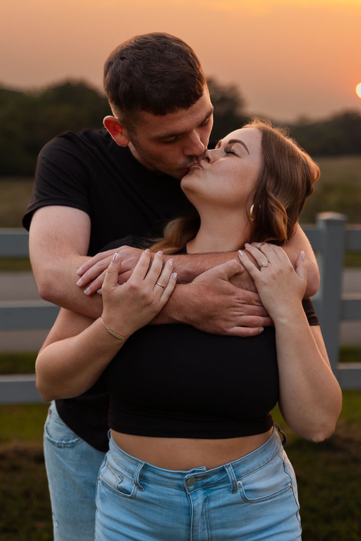 A romantic couple shares tender kisses at golden hour in a scenic outdoor setting.