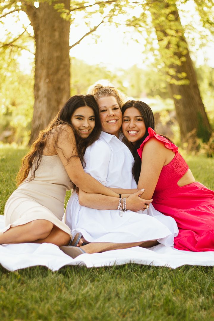 A family wearing white and red outfits lies together on a blanket in a sun-drenched park setting.