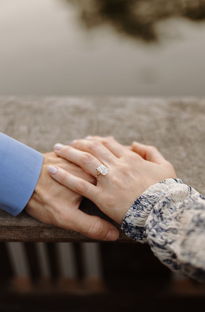 Close up shots of hands with engagement ring resting on rustic wooden railing.