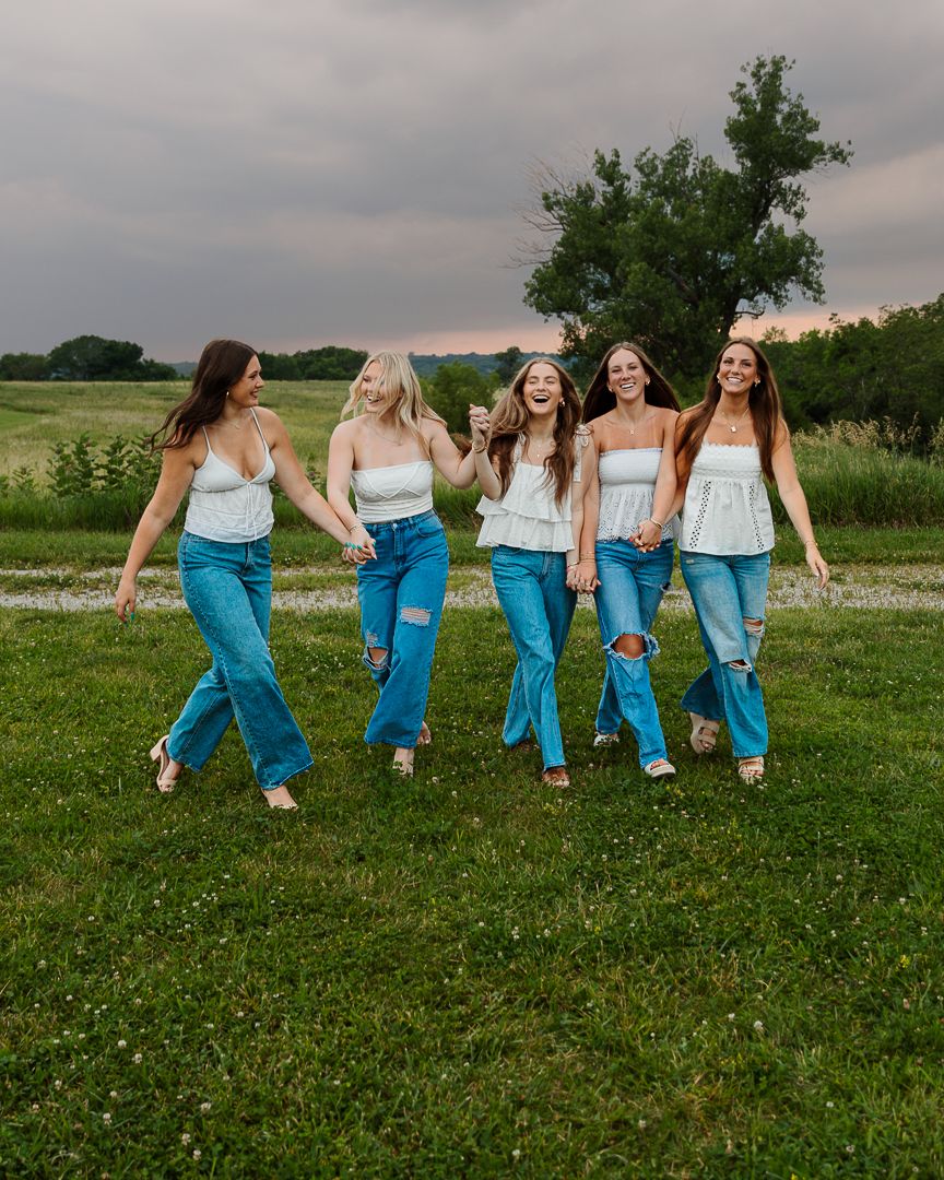 A group in white tops and blue jeans walks together across a grassy field at sunset.