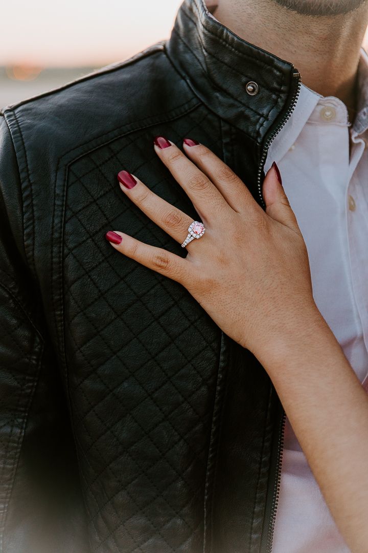 A hand wearing red nail polish touches a black quilted leather jacket over a white shirt.