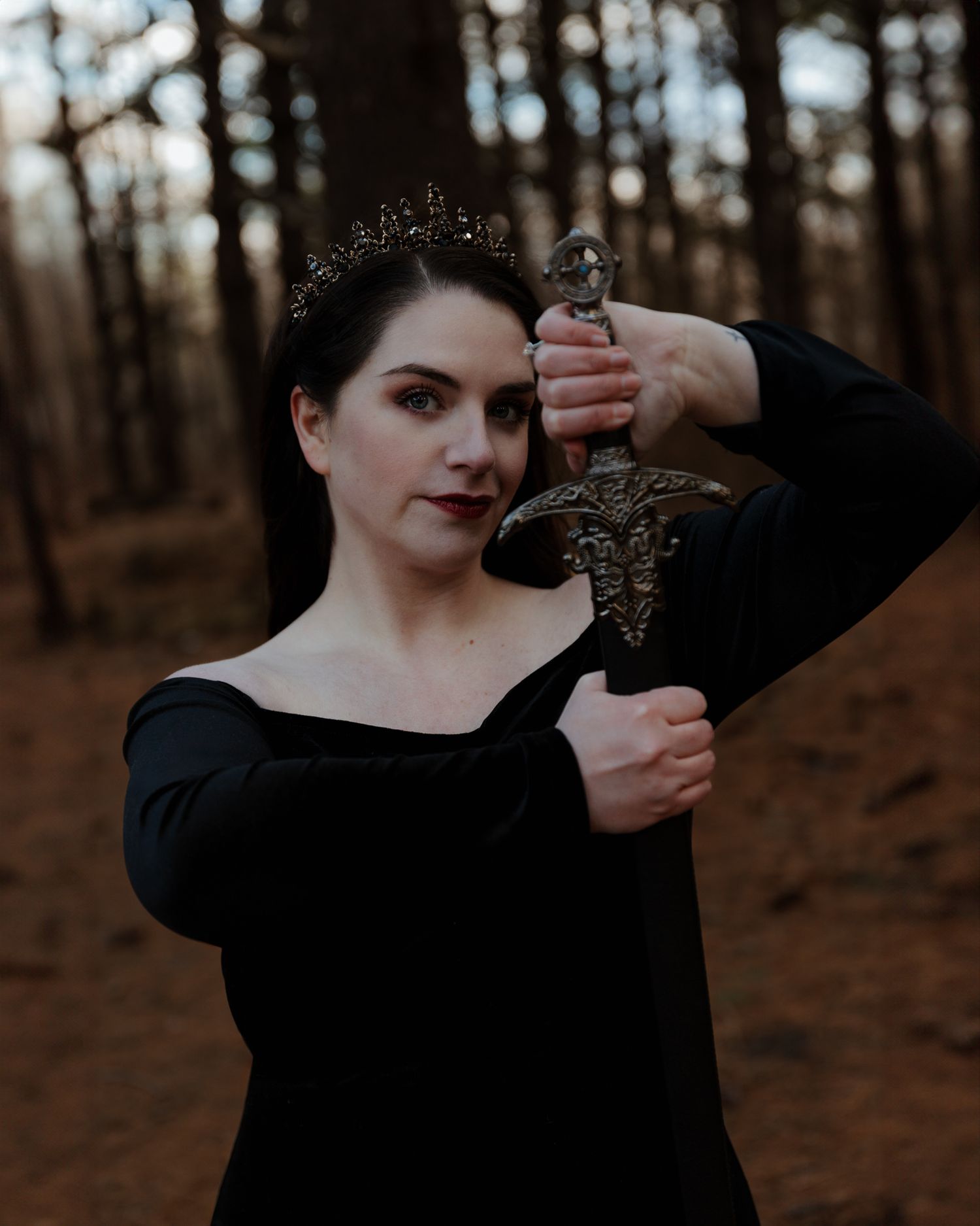 Gothic styled portrait in black attire against a moody forest backdrop.
