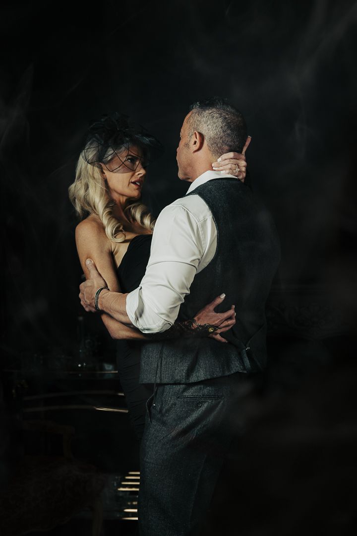 Dramatic low-light dance scene with couple in formal attire against dark background.