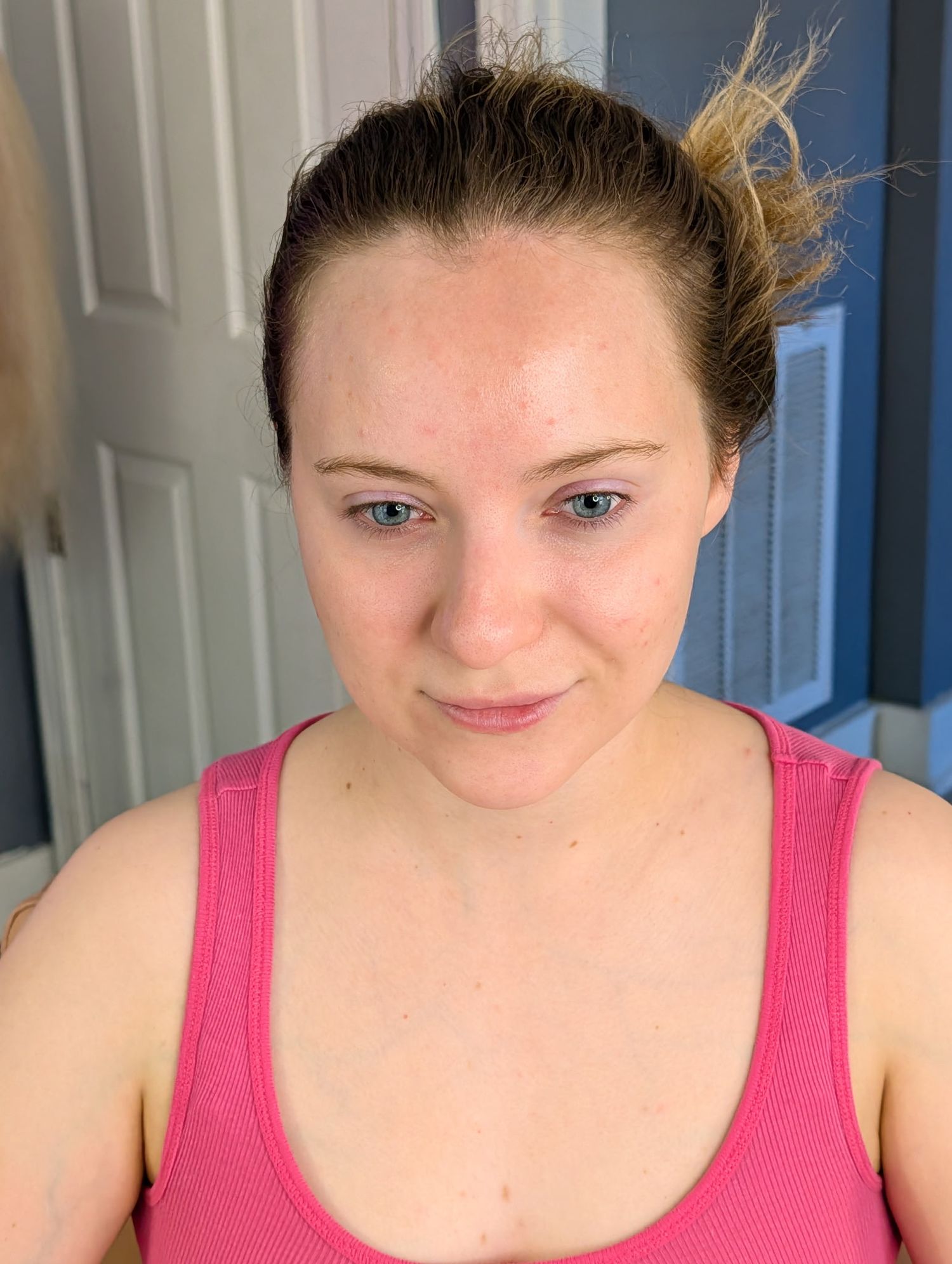 Young woman with blue eyes and brown hair in a pink tank top poses indoors near a blue door.