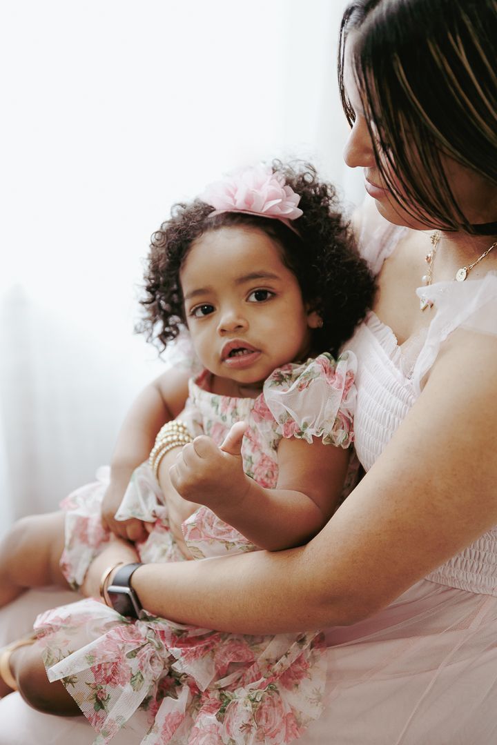 Sweet tender moment captured between parent and child in soft pink hues with delicate lace details.