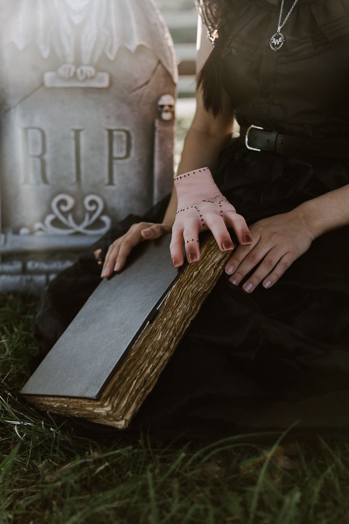 Hands rest on an ancient book beside a RIP gravestone in a moody cemetery setting.