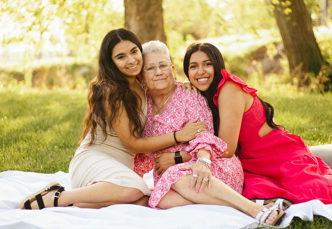 Three people in pink and red clothing laying on grass during a bright sunny outdoor photo session.