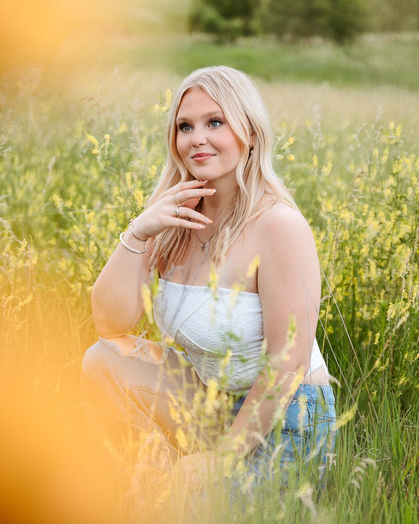 Person in blue floral top poses among yellow wildflowers at golden hour.
