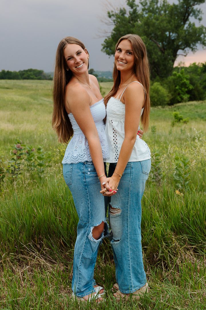 Friends wearing white tops and denim pose playfully together in a green summer field.