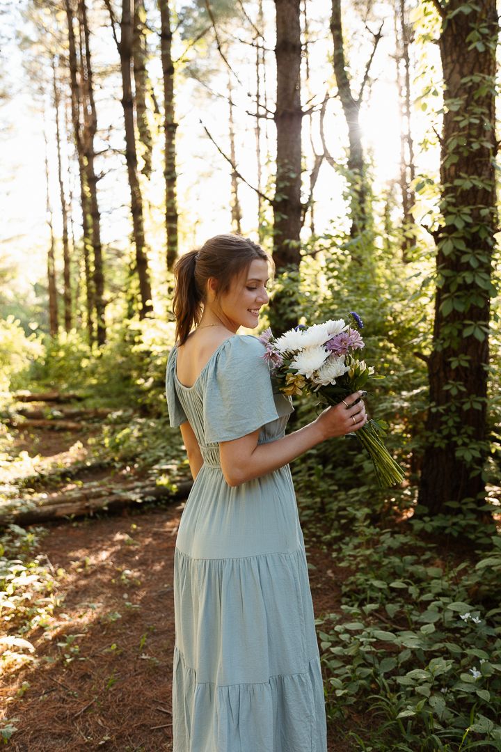 Flowing light blue dress stands out against golden sunlit forest backdrop while gathering flowers.