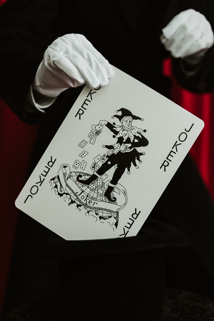 Magician in white gloves holding a large Joker playing card during a magic trick performance.