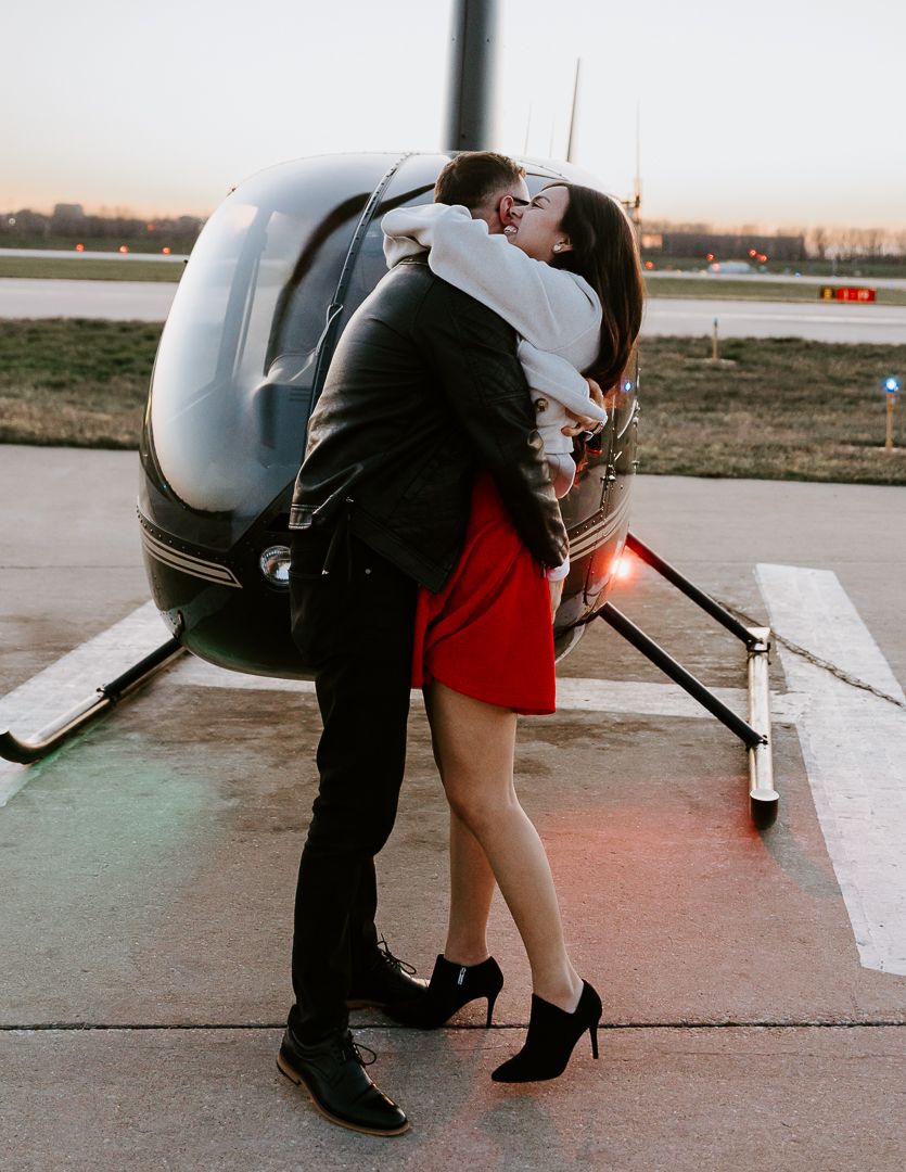 A couple bending down together near a small aircraft on an airfield at sunset.