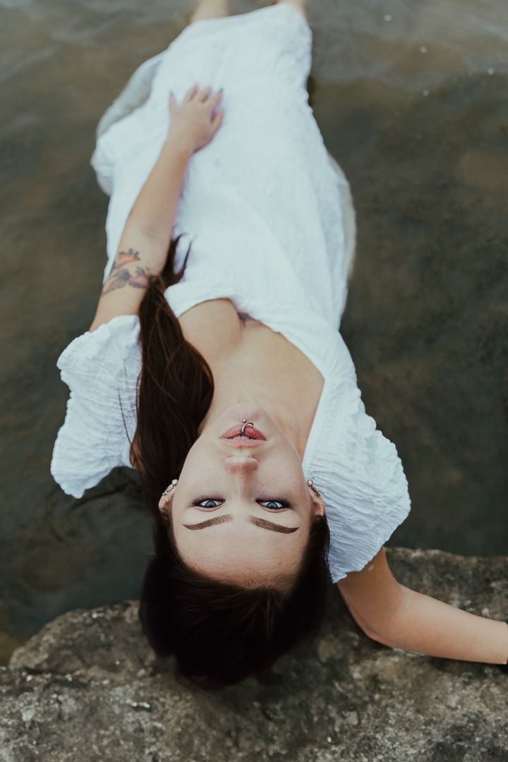 Artistic portrait of someone lying on concrete in a flowing white dress with dramatic lighting.