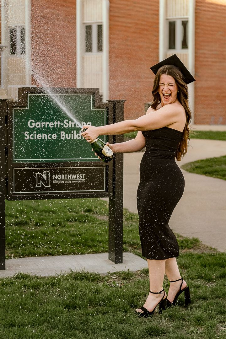 A happy woman in a black dress poses with playful energy next to a Garrett Strong Science Building sign on a college campus.