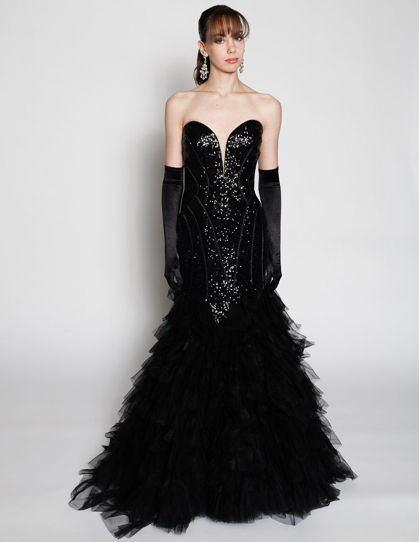 Black sequin strapless mermaid gown with ruffled tulle skirt and long gloves on a model.