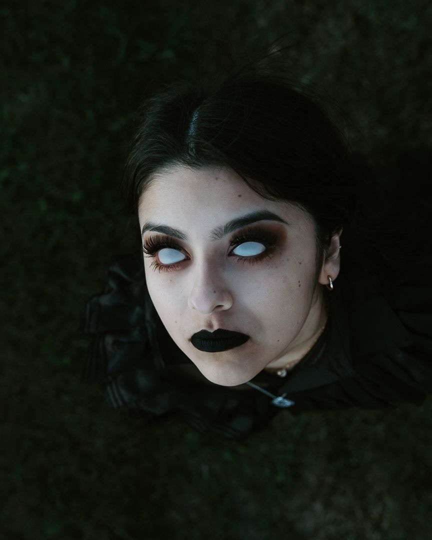 Gothic-style portraits in dark lighting show dramatic makeup with black lipstick and pale white contact lenses.