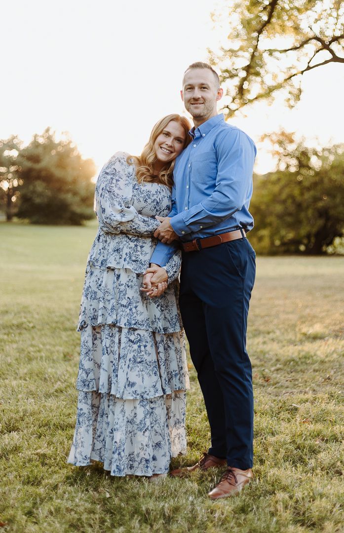 Couple embraces in golden sunset light wearing coordinated blue and floral outfits for engagement photos.