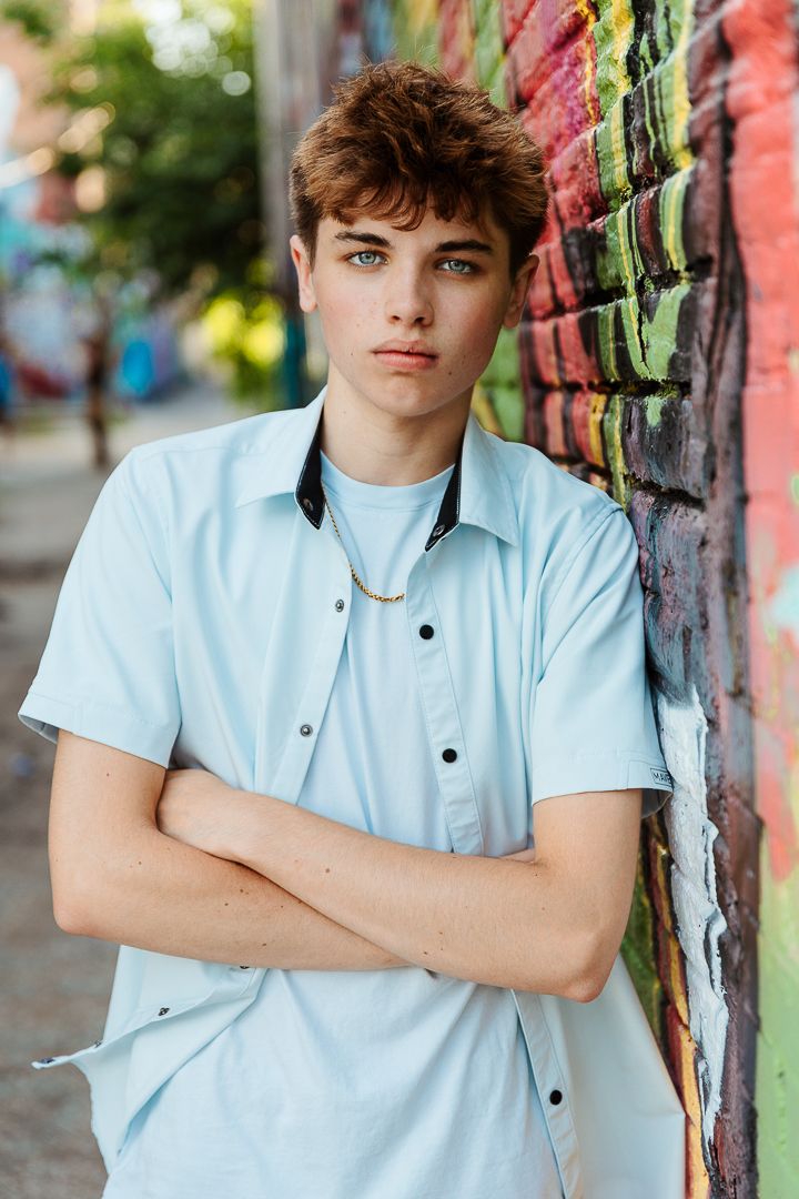 Person in light blue polo shirt poses against colorful graffiti wall in urban setting.