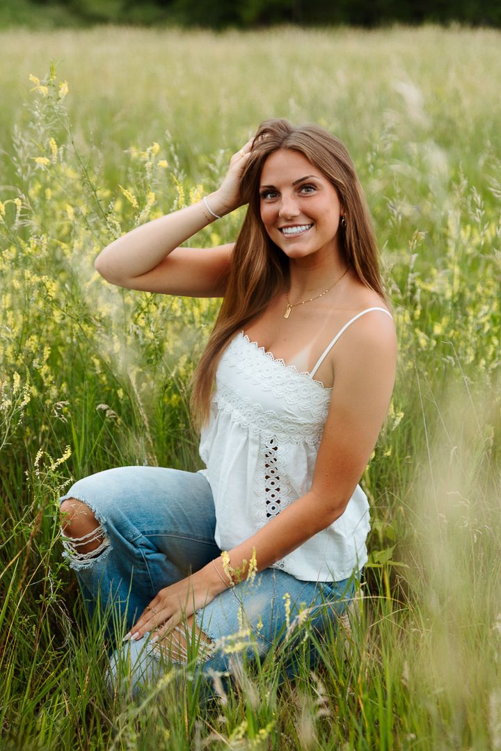 Woman in white top and jeans poses gracefully in field of yellow wildflowers.