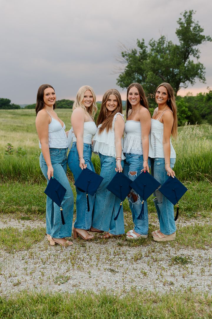 Five people wearing matching light blue tops and jeans pose together on a gravel path near a grassy field.