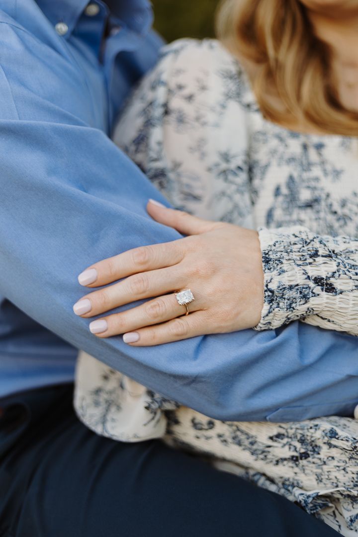 Close-up photo of hands with engagement ring on a blue and floral fabric background showing love and commitment.