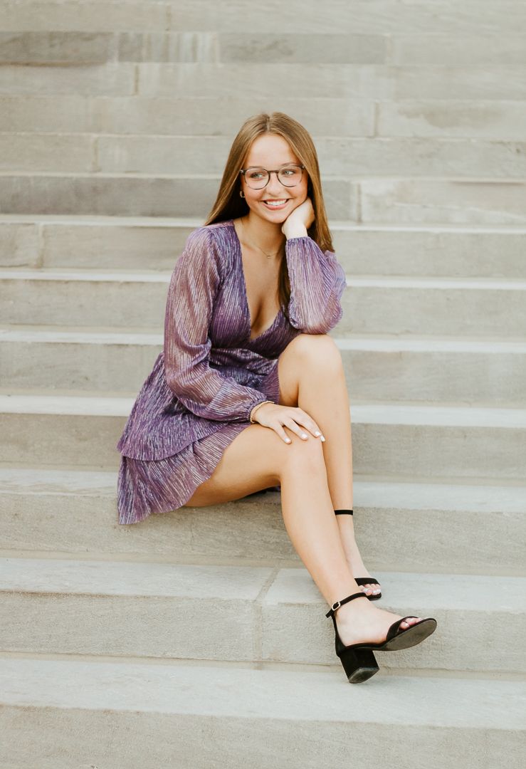 A person in a purple dress and glasses sits casually on concrete stairs in various relaxed poses.