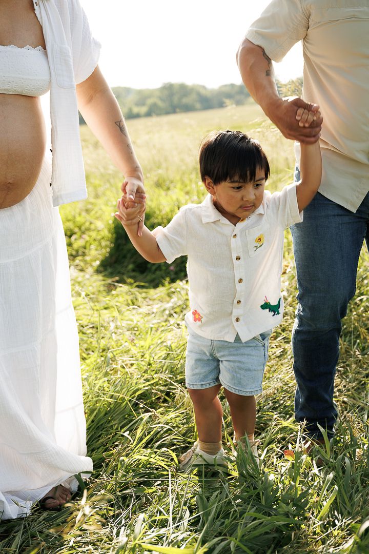Lower body view of a family standing together in a grassy field during golden hour.