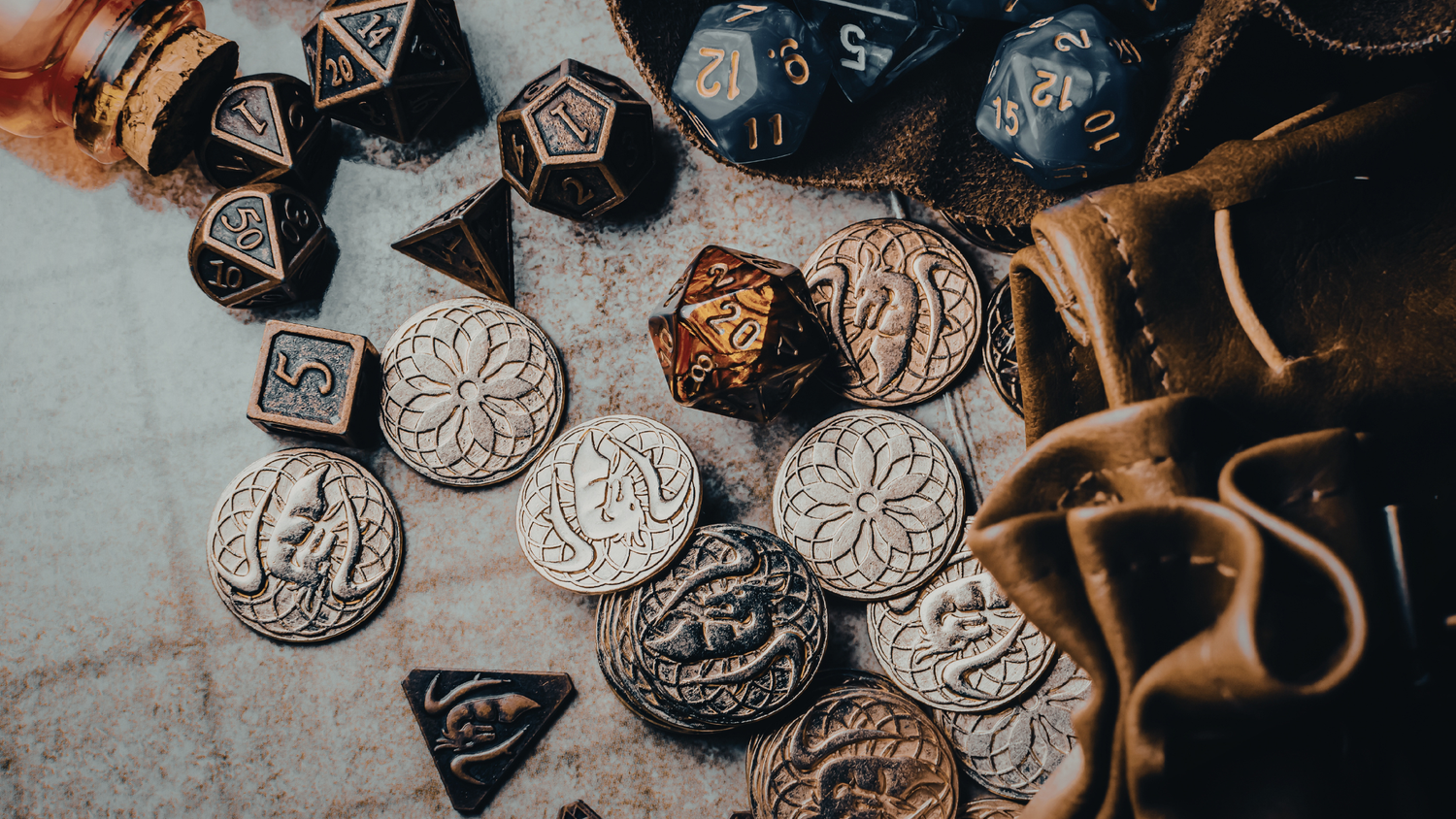 A collection of polyhedral gaming dice and silver coins arranged with wooden branches on a textured surface.