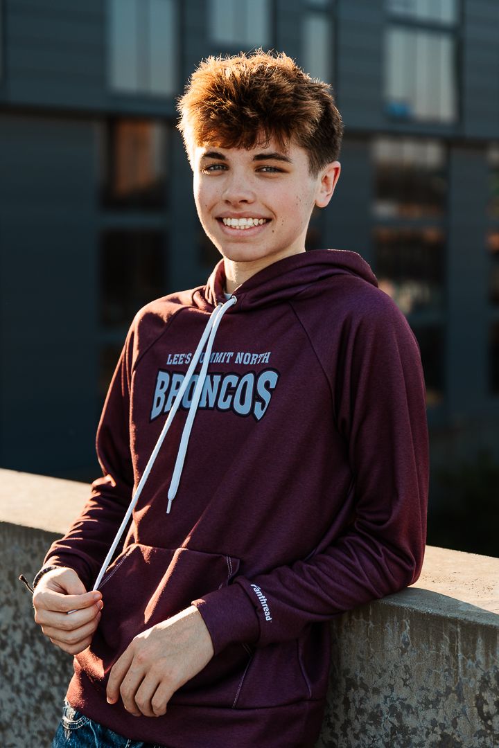 Person wearing purple hoodie sits outside at sunset on concrete ledge.