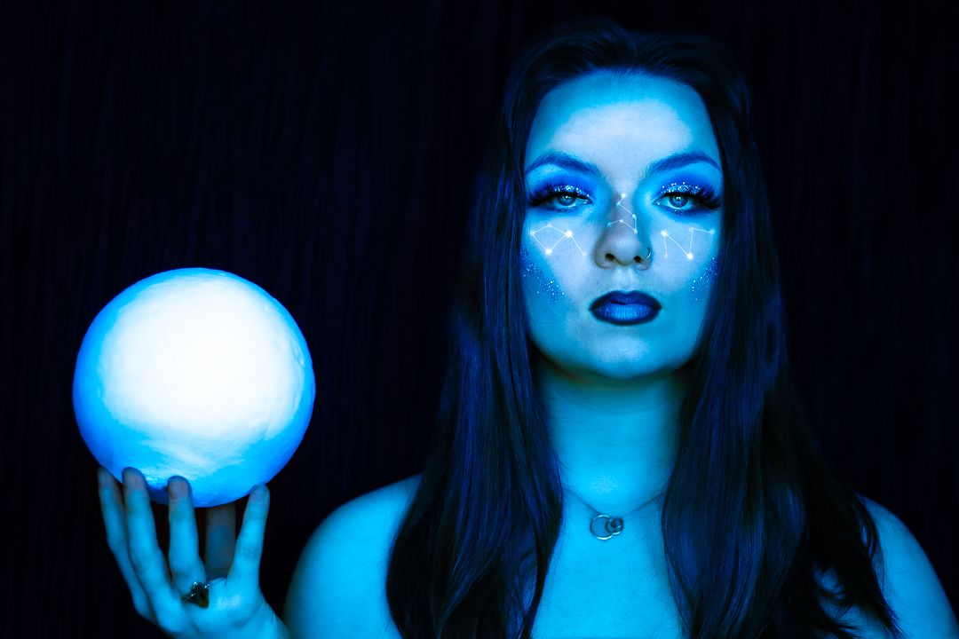 A mystical portrait in blue lighting shows someone holding a glowing orb against a dark background.