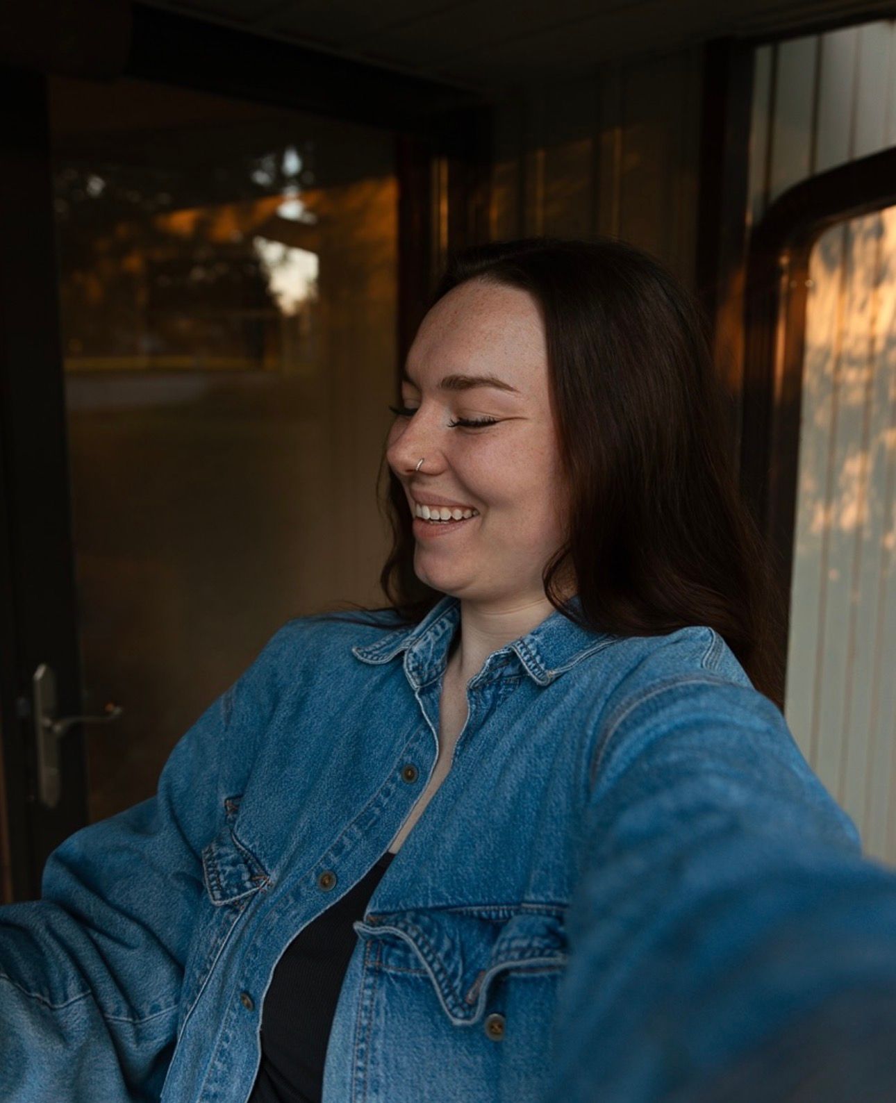 A person wearing a denim jacket sits by a window with natural light streaming in, creating a warm atmosphere.