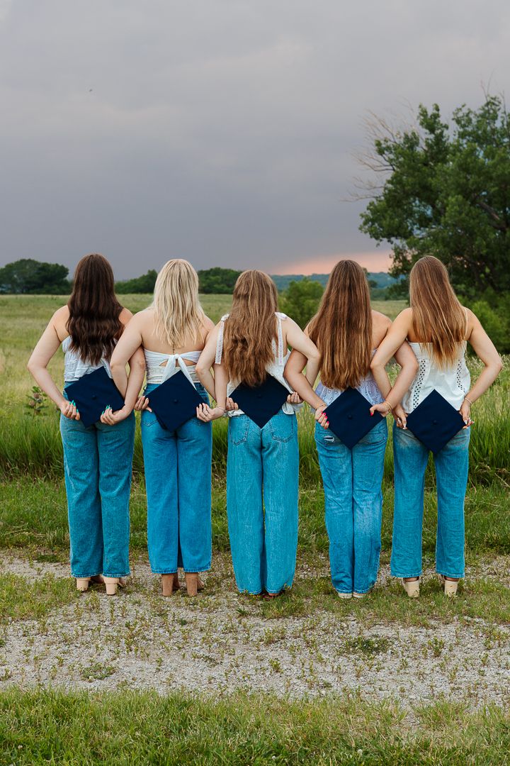 A group wearing matching denim overalls sits together in a row on grass with their backs to the camera.
