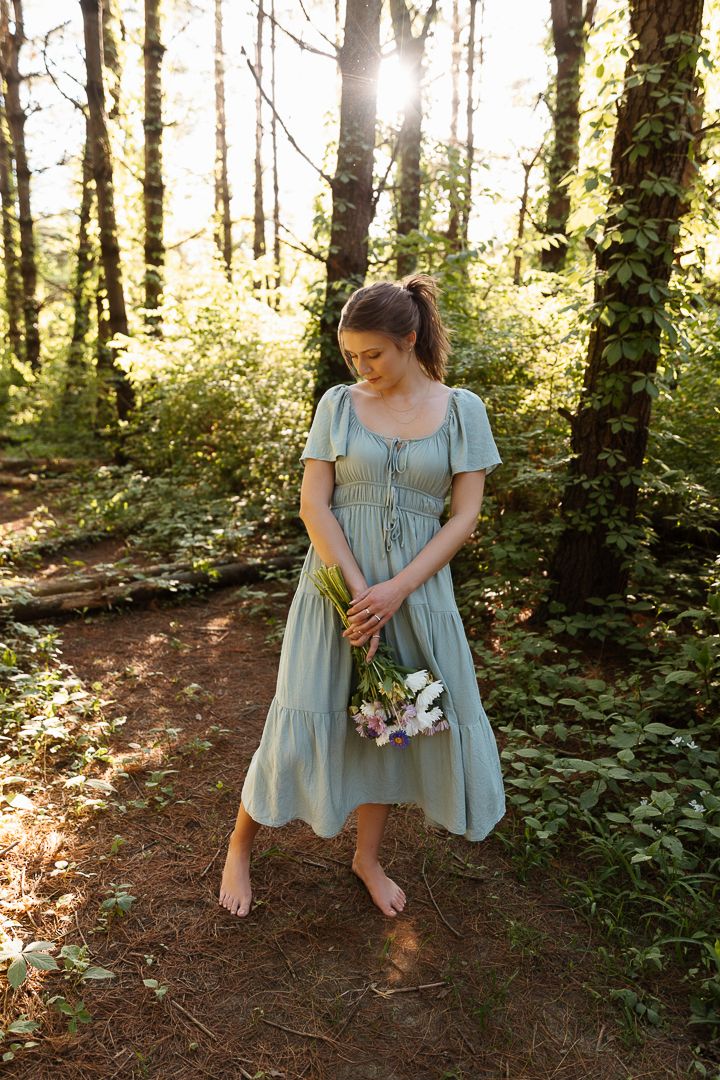 Ethereal forest photoshoot featuring a sage green dress and dappled sunlight through the trees.