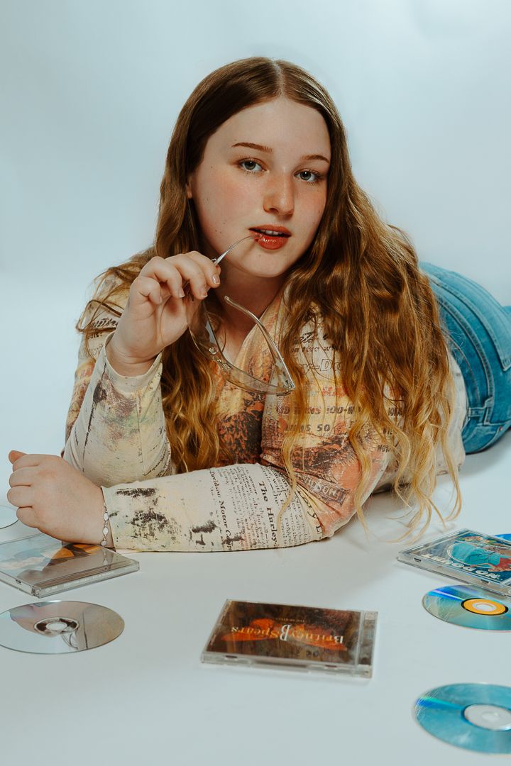 Artistic portrait with long wavy hair looking at vintage CDs and records on white surface with dreamy lighting.