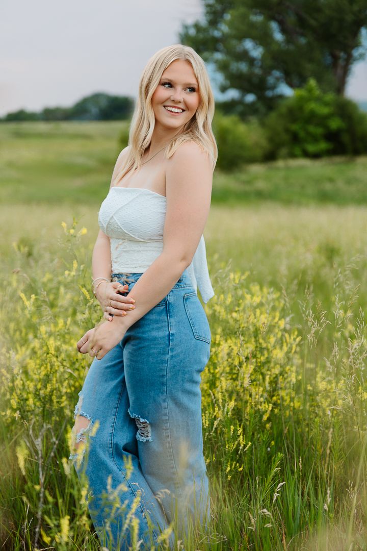 Woman poses in a white top and overalls in a sunny wildflower field during a summer photo session.