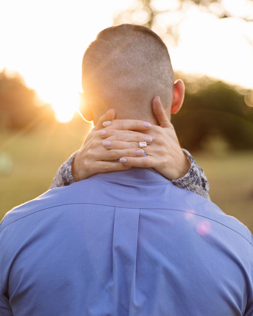 Romantic sunset engagement photo showing clasped hands with diamond ring against golden light.