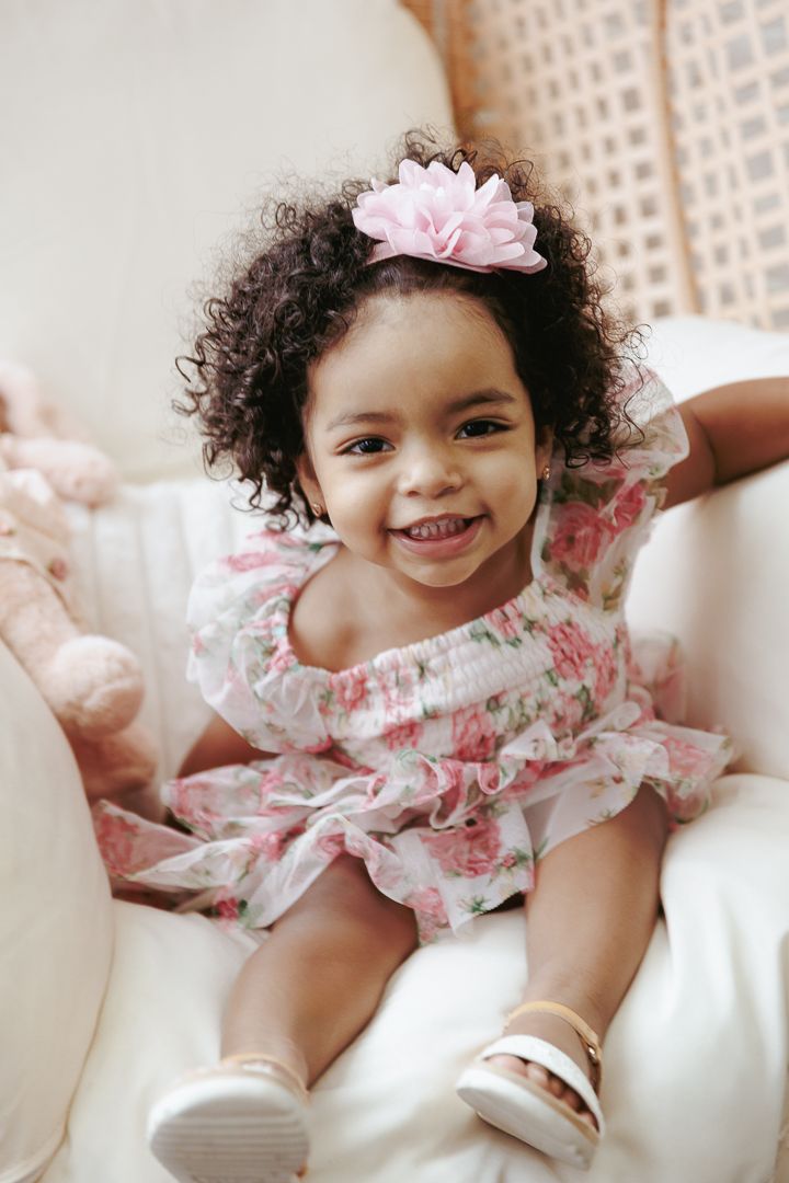 Three joyful photos show a baby wearing a pink and white ruffled dress while playing on white cushions.