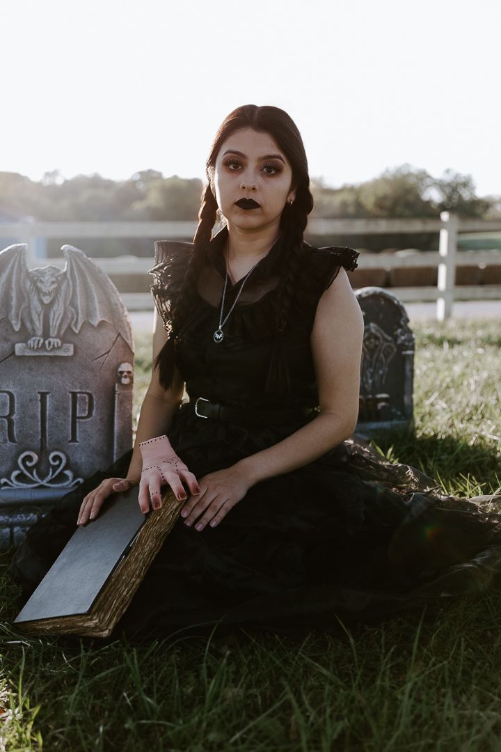 Gothic style portrait in a cemetery with dark clothing, vintage book and gravestones at sunset.