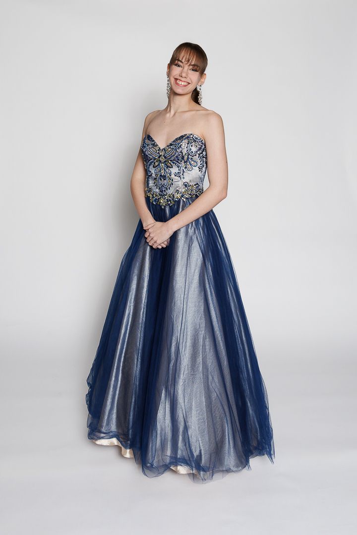 Woman smiling in a strapless navy blue ball gown with silver embroidery and tulle skirt.