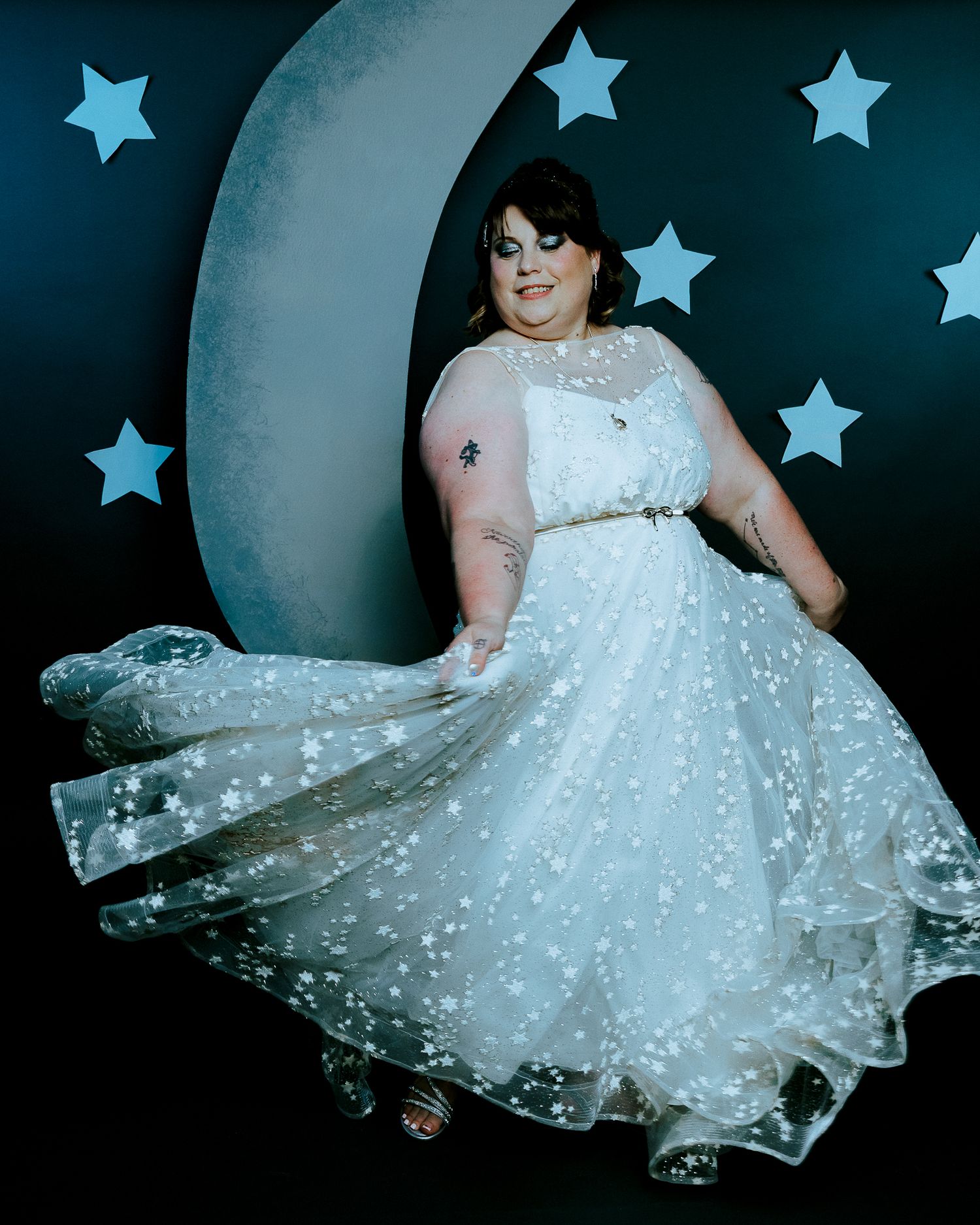 Plus-size bride twirling in a star-print white gown before a crescent moon backdrop with blue stars.