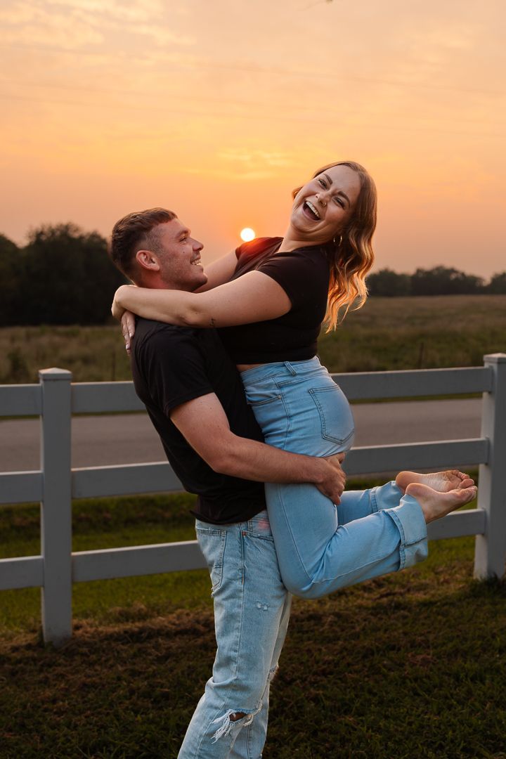 A couple shares an intimate moment together during sunset by a white fence.
